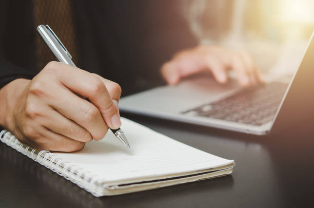 istock person man holding pen write plan or idea on book with computer laptop on desk. 1411660542
