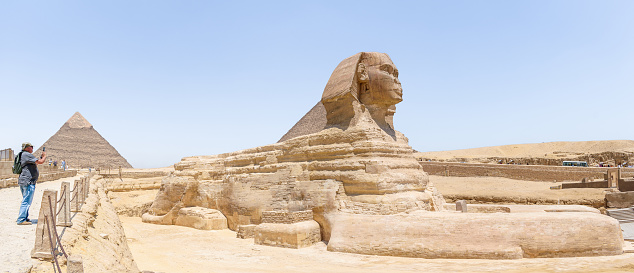 The Great Sphinx of Giza, Giza Necropolis, Egypt - July 27, 2022:  The Great Sphinx of Giza is a limestone statue of a reclining sphinx, a mythical creature with the head of a human, and the body of a lion. Facing directly from west to east, it stands on the Giza Plateau on the west bank of the Nile in Giza, Egypt. The face of the Sphinx appears to represent the pharaoh Khafre.\n\nThe original shape of the Sphinx was cut from the bedrock, and has since been restored with layers of limestone blocks. It measures 73 m (240 ft) long from paw to tail, 20 m (66 ft) high from the base to the top of the head and 19 m (62 ft) wide at its rear haunches.[4] Its nose was broken off for unknown reasons between the 3rd and 10th centuries AD.\n\nThe Sphinx is the oldest known monumental sculpture in Egypt and one of the most recognisable statues in the world. The archaeological evidence suggests that it was created by ancient Egyptians of the Old Kingdom during the reign of Khafre (c. 2558–2532 BC).