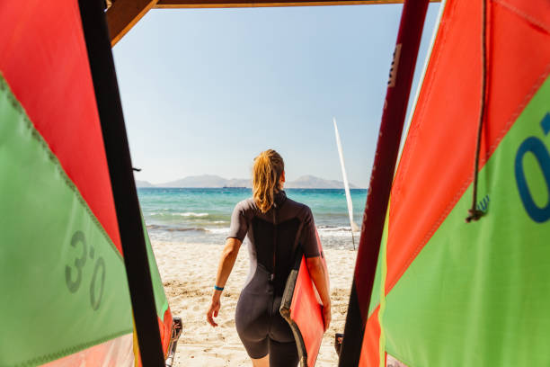 An adventurous young woman carrying a surfboard while walking on sand