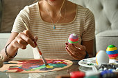 istock Close up of Asian female painting multi-colored Easter eggs with paintbrush and colour palette at home. 1411664869