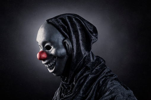 Scary clown showing his teeth over dark misty background