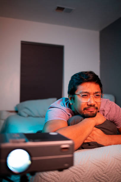 istock (Cringing) Man Watching a Movie in Bed with Projector 1411669138