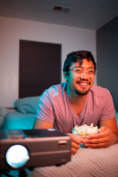 istock (Laughing) Man Watching a Movie in Bed with Projector 1411670838