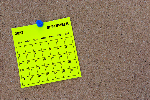 September 2023 yellow sticky note calendar with pin on cork bulletin billboard. Copy space.