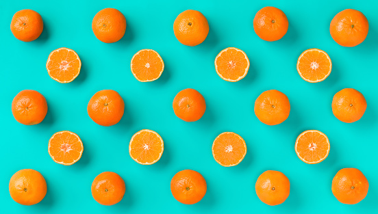 Fruit pattern of fresh mandarin slices on blue background. Flat lay, top view. Pop art design, creative summer concept. Half of citrus in minimal style. Tangerine.