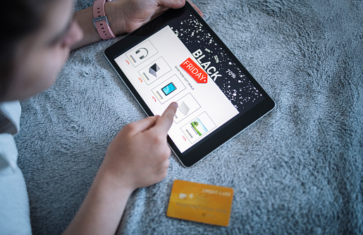 Young woman laying on bed using digital tablet and credit card to make a online purchase for electronics on sale. Black Friday sale.