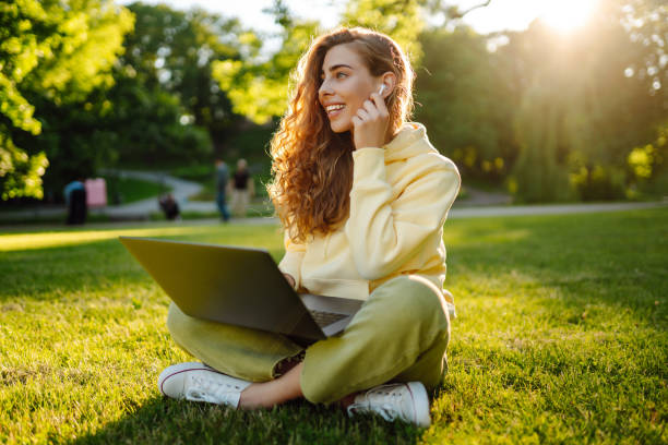 Young woman with laptop sits on the grass in the park on a sunny day. stock photo