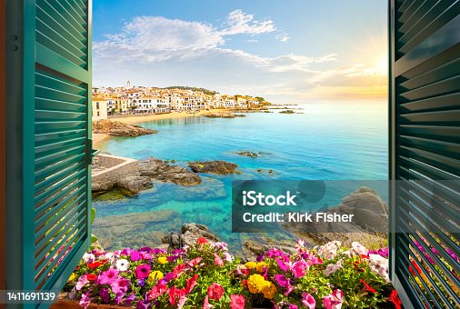 istock View through an open window with shutters of the sandy beach, rocky coastline and whitewashed town of Calella de Palafrugell, Spain, on the Costa Brava coast as the sun sets. 1411691139
