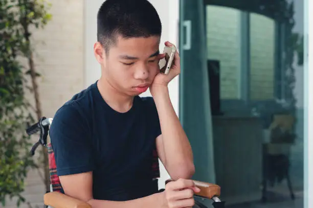 Photo of Teenager boy with disability on wheelchair using phone for call.