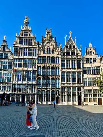 Two women taking a selfie on Grote Markt in Antwerp. The Great Market Square is filled with numerous elaborate 16th century guildhalls.