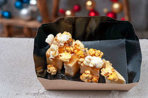 cheesecake with salted caramel and popcorn in a black paper package for delivery against the background of Christmas balls close-up.