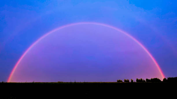 istock a bright rainbow on a dark background of trees and fields 1411696665