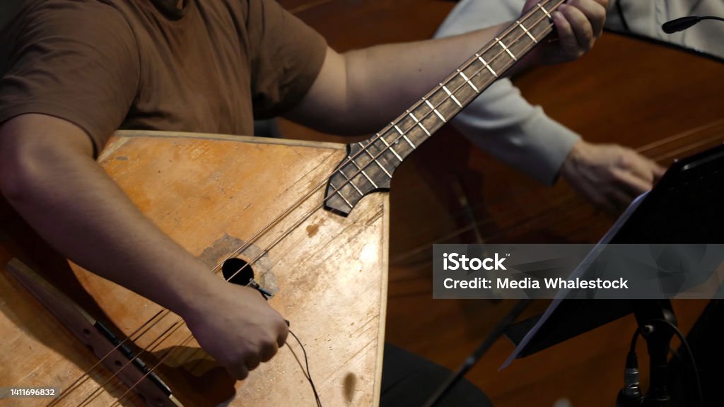 Balalaika wooden in the hands of the musician. Folk musical art of the rural traditional. Man plays the Balalaika-contrabass Balalaika wooden in the hands of the musician. Folk musical art of the rural traditional. Man plays the Balalaika-contrabass. Acoustic Guitar Stock Photo