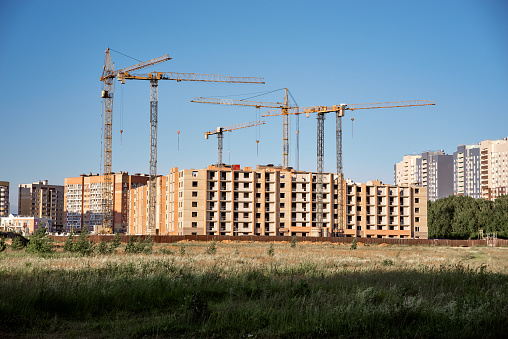 Construction of a new residential district with buildings and cranes. Construction site, blue sky, grass area in front