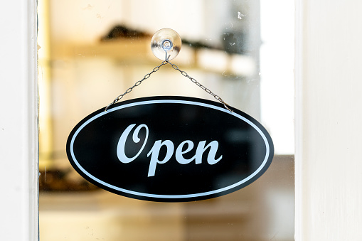 Shop door oval open sign hanging on glass entrance to retail business interior blurred in background