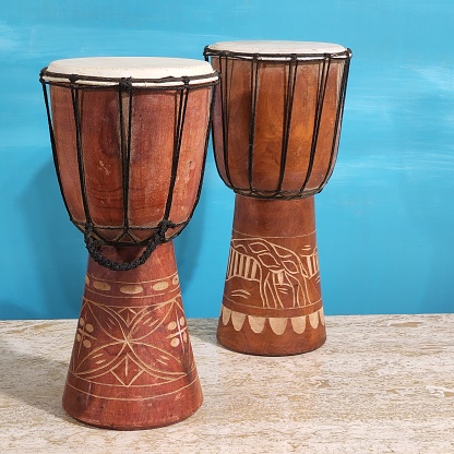 Pair of wooden bongo drums with handing carvings.  Turquoise background.  Sitting on marble top table.  African drums.