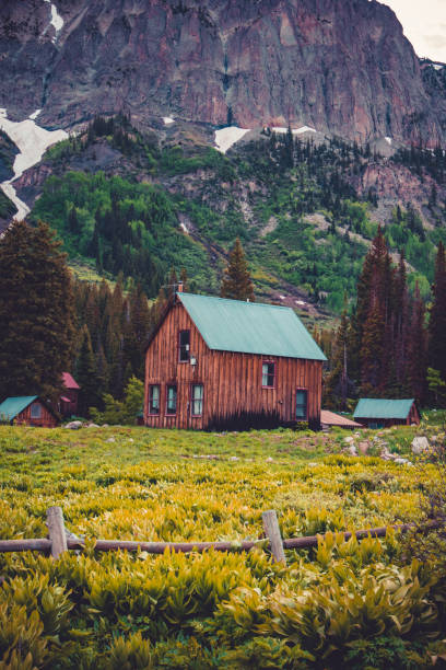 A wooden cabin stands in a lush green meadow near Lautersee in Upper Bavaria, Germany. Surrounded by forest and mountains, the scene is illuminated by bright sunlight breaking through dramatic clouds. A peaceful rural landscape in the Bavarian Alps.
