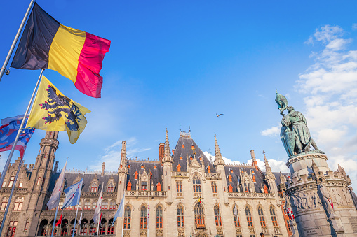 Belgian and euro flags with flemish architecture in Bruges\n\nThe flags are the symbol of Bruges, made by the munipality for the city.\n\nThe Provinciaal Hof (Province Court) is a Neogothical building on the market square. It is the former meeting place for the provincial government of West Flanders. The national government owns the building.\n\nThe Market Square , in the shadow of the majestic belfry tower, was the scene of medieval festivals, fairs, tournaments, uprisings and executions. \n\nToday, the square serves as e meeting place for the locals and the three to four million visitors who flock to the town every year. \n\nThe statues at the centre of the square are of Jan Breydel and Pieter de Coninck, two freedom heroes in the struggle against the French at the beginning of the 14th century. Jan Breydel was head of the butchers and Pieter de Coninck was head of the weavers. The statue was erected in 1887.