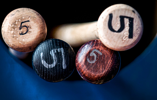 Group of Wooden Baseball Bats in a dugout batting rack with hand lettering of player number to designate team player