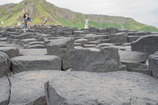 Hexagonal columns of basalt, cliff face and tourists (out of focus) at the shoreline of the Giant's Causeway, County Antrim, Northern Ireland.  The site is a UNESCO World Heritage Site.