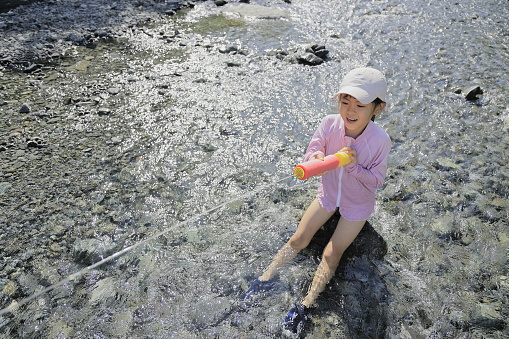 Japanese student girl playing in the river with water gun (7 years old)