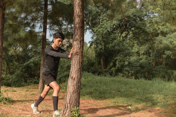 istock A young asian man stretches his calves while leaning on a pine tree. A morning warmup before a running session. 1411729084