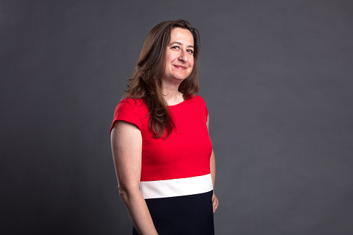 Studio portrait of middle-aged white woman wearing a red, white and black dress posing against a gray background.