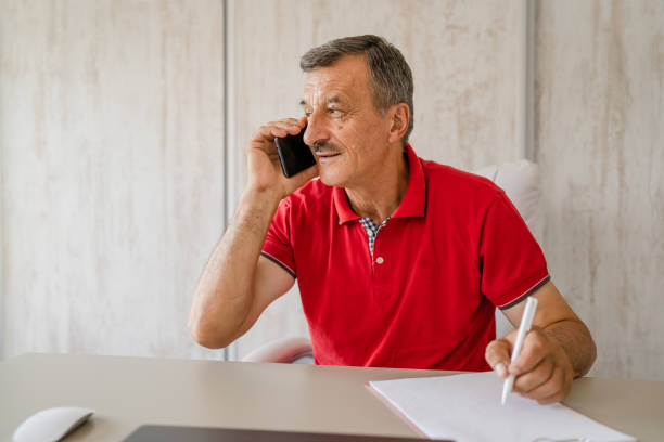 istock one man senior entrepreneur active caucasian male making a phone call talking while sitting at the desk table working at office manager and small business real people copy space 1411740823
