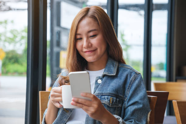 istock Portrait image of a young woman holding and using mobile phone while drinking coffee in cafe 1411748165