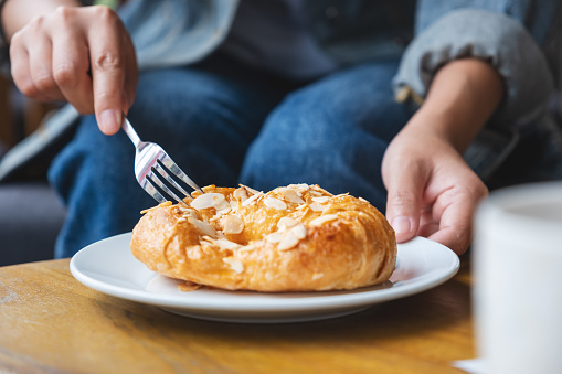 Closeup image of a woman holding and eating a fresh almond croissant with fork