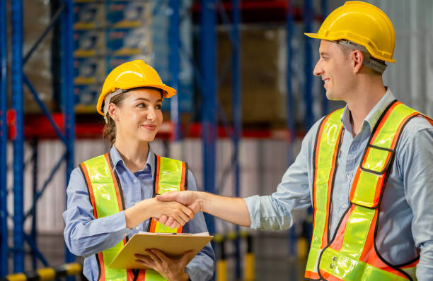 trabajador del almacén estrechando la mano de su colega en el almacén industrial, trabajador de uniforme estrechando la mano del capataz en el almacén de la fábrica - hardhat construction men handshake fotografías e imágenes de stock