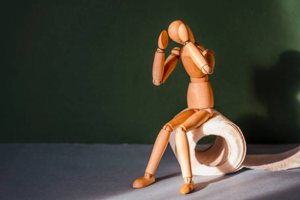 Wooden figure sit on a roll of toilet paper. Concept of the problem with digestion. stock photo