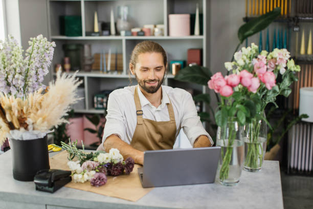 istock Portrait of attractive man florist working on computer at workplace. 1411759623