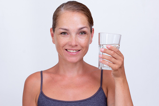 Caucasian beautiful middle aged woman of 40s holding glass of pure water on white background looking at camera