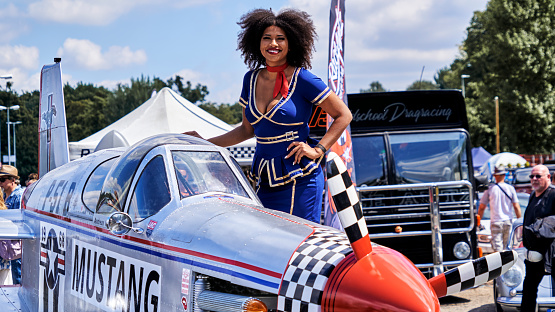 Hannover, Germany, July 23, 2022: Mustang converted from Ford sports car to airplane with smiling pretty young black woman in blue uniform