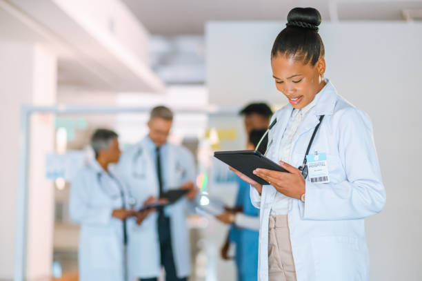 istock Female doctor using a digital tablet with blurred colleagues in the background. Modern healthcare professional or physician checking or reviewing patient medical records on software app at a hospital 1411766676