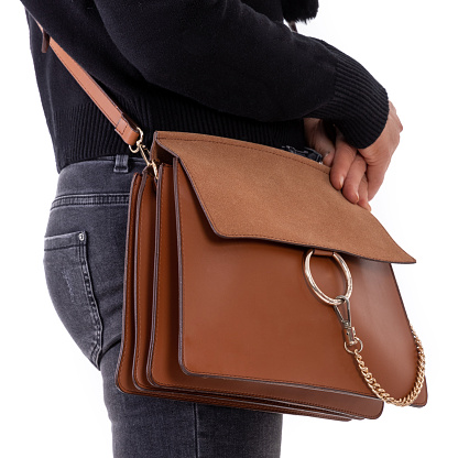 Every detail counts. Stylish woman in black jeans with leather bag over her shoulders, holding it on her hips.