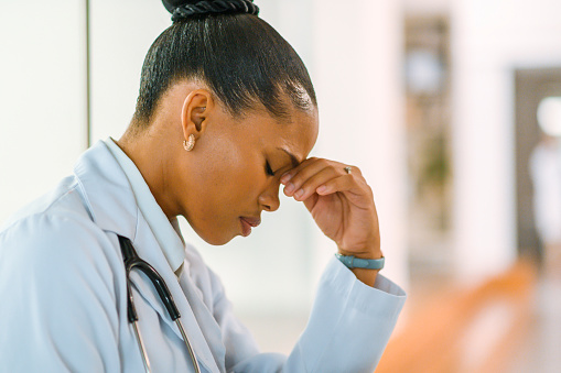 Stressed and unhappy doctor feeling anxious, worried and frustrated while working in a hospital. Female practitioner looking hopeless while struggling with burnout, headaches and medical challenges
