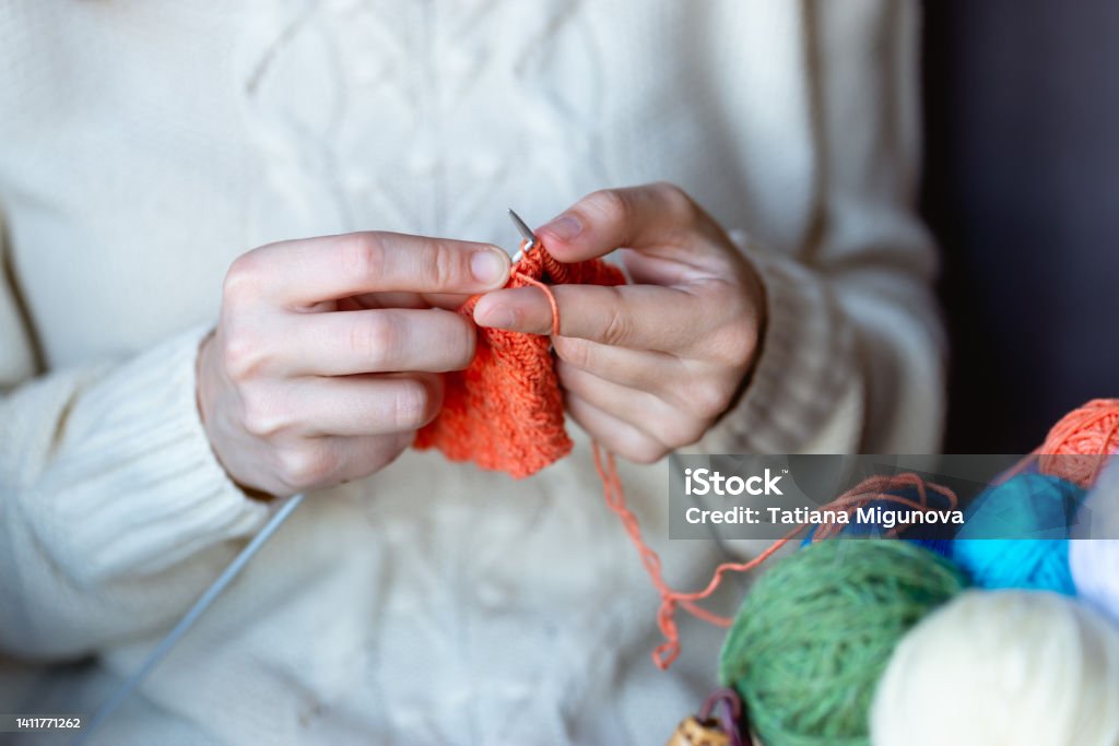 A girl in a white sweater knits with knitting needles. Women's hands knit with knitting needles. Needlework, knitting. Handmade work. Hobby. Horizontal photo. Ball Of Wool Stock Photo