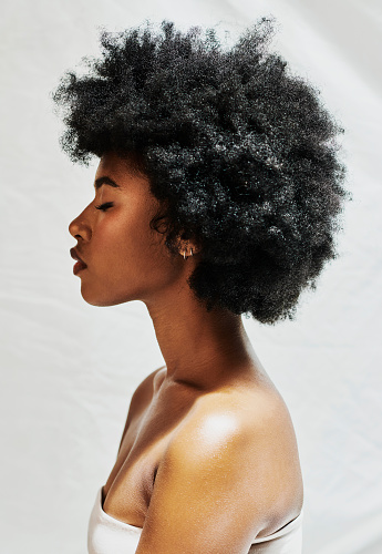 Side profile of an african woman with a afro isolated against a white background in studio. Beautiful female with curly hair showing perfect skin for cosmetics, and natural beauty for makeup products