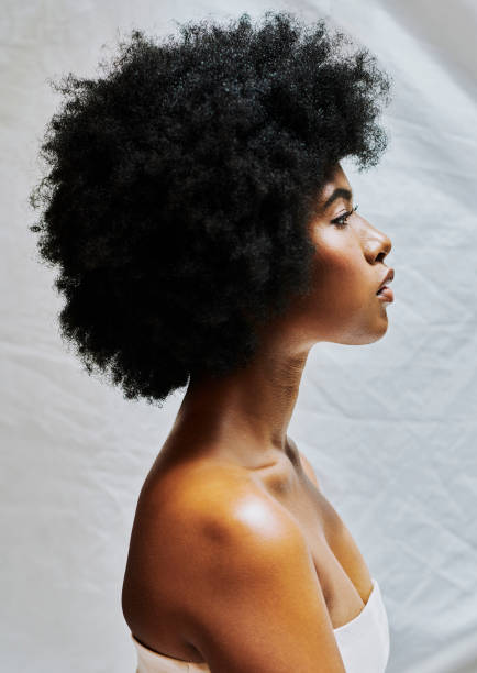 side profile of african woman with afro isolated against a white background in a studio. beautiful female with curly hair showing perfect skin for cosmetics and natural beauty for makeup products - afro stockfoto's en -beelden
