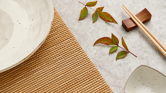 Chopsticks and japanese empty plate and nandina leaves on retro gray table - top view