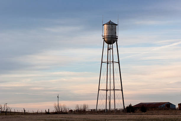 Old small town water tower in western/southwestern USA. Tower is lit from the left side by the setting sun and is set against a cloudy sky at sunset.