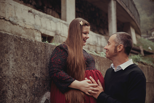 Beautiful couple portrait smiling at each other while touching pregnant belly