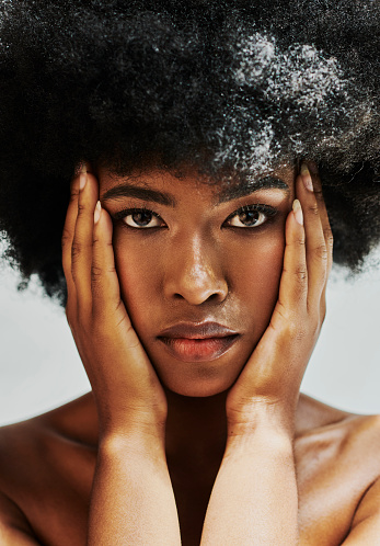 Closeup up of beauty African woman with black afro touching her face. Face of beautiful edgy black female feeling her flawless and soft skin. Serious woman satisfied with skin after spa treatment