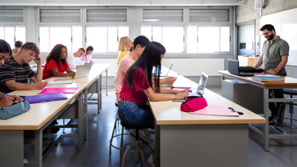 istock Side view of group of multiracial students studying and using laptops in class with male teacher. 1411780011