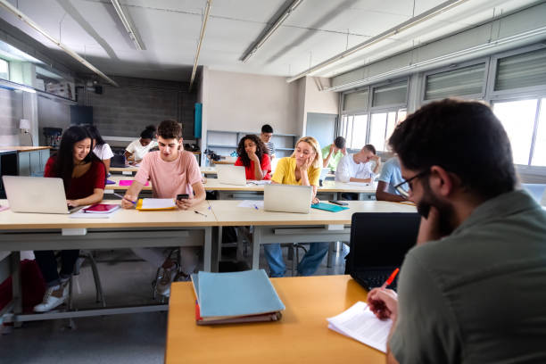 istock Male caucasian teacher marking exams while multiracial students studying and using laptops in class. 1411780045