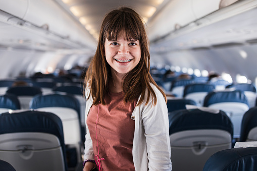 Smiling girl wearing dental braces standing in a plane and listening to music