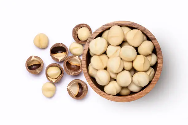 Macadamia nuts in wooden bowl isolated on white background, top view, flat lay.