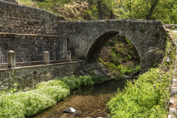 istock Rustic stone arch and wall with footpath over calm creek 1411802592